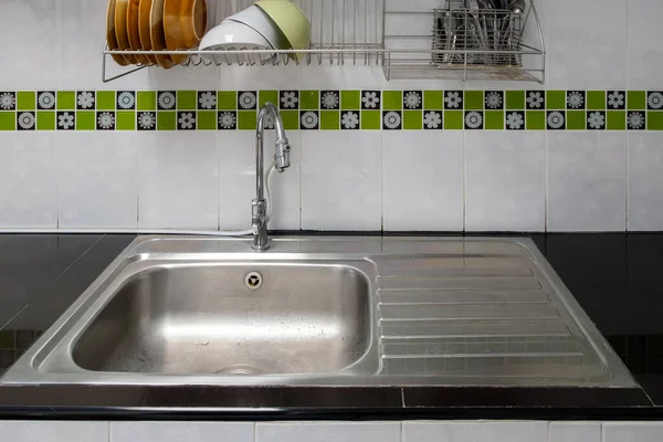 The modern sink on the black counter with the stainless steel rack for dish drainer, front view with the copy space.