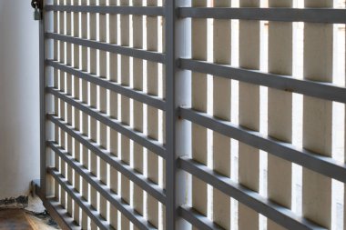 The metal fence gate is decorated with white slats on the slide of the urban house, front view with the copy space