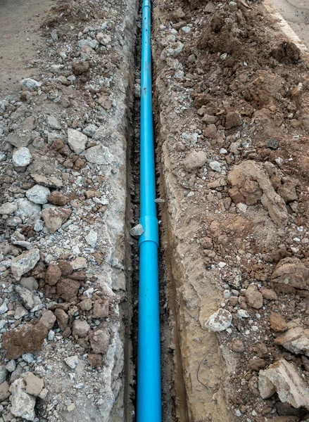 The new PVC pipe is laying in the trench near the asphalt road for the water supply system of the rural village, front view with the copy space.