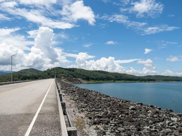 The asphalt road along the large earth dam for hydroelectric power generation in the northern part of Thailand, front view with the copy space.