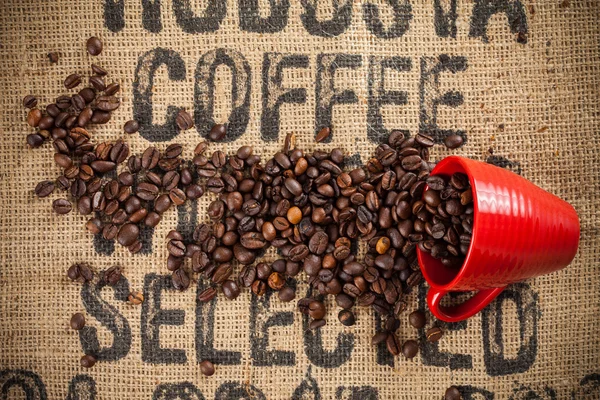 Spilled coffee beans and red cup — Stock Photo, Image