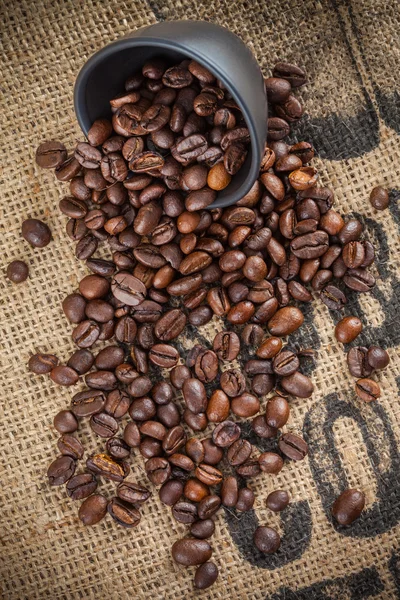 Spilled coffee beans and black cup, top view — Stock Photo, Image