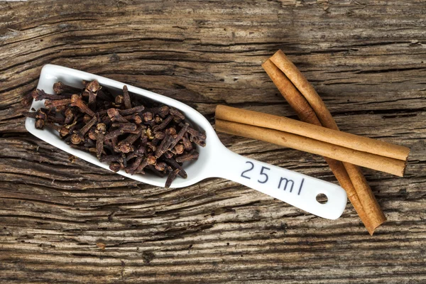 Cloves in the scoop, two cinnamon barks on the old wood background — Stock Photo, Image