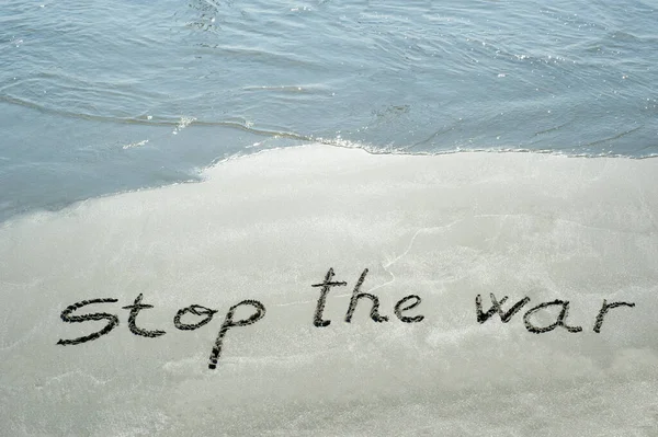 Concept or conceptual Stop de war  handwritten text in sand on a beach with waves in an exotic island for no war, freedom and safety, protest, activism, patriotism, message, nature and peacefulness