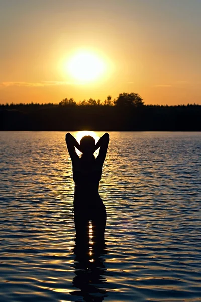 Flickan står i sjön vid solnedgången — Stockfoto