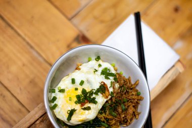 Indonesian fried noodles with fried egg and red chili and green onions served in a bowl with chopsticks with a red napkin. With high angle