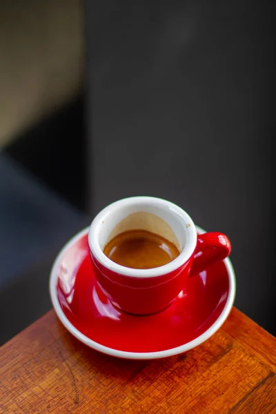 Photo of espresso coffee in red cup on end of vintage wooden table with top view.