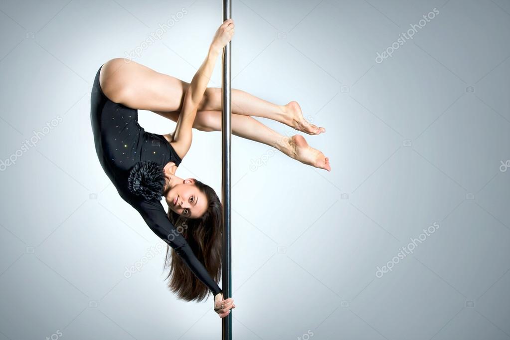 Young sexy woman exercise pole dance against a gray background