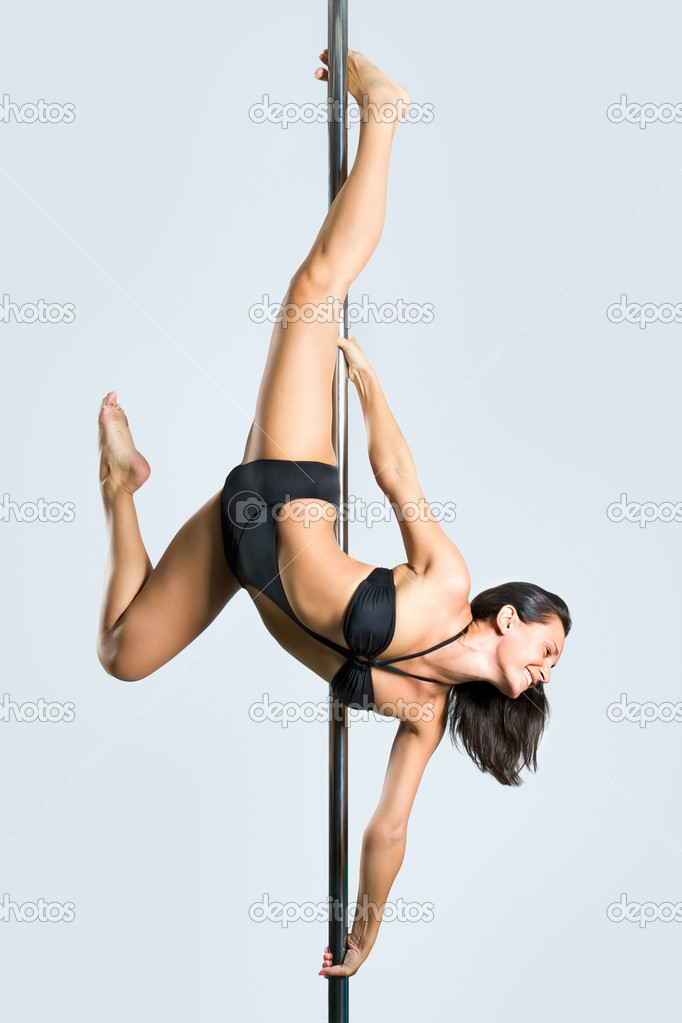 Young sexy woman exercise pole dance against a gray background