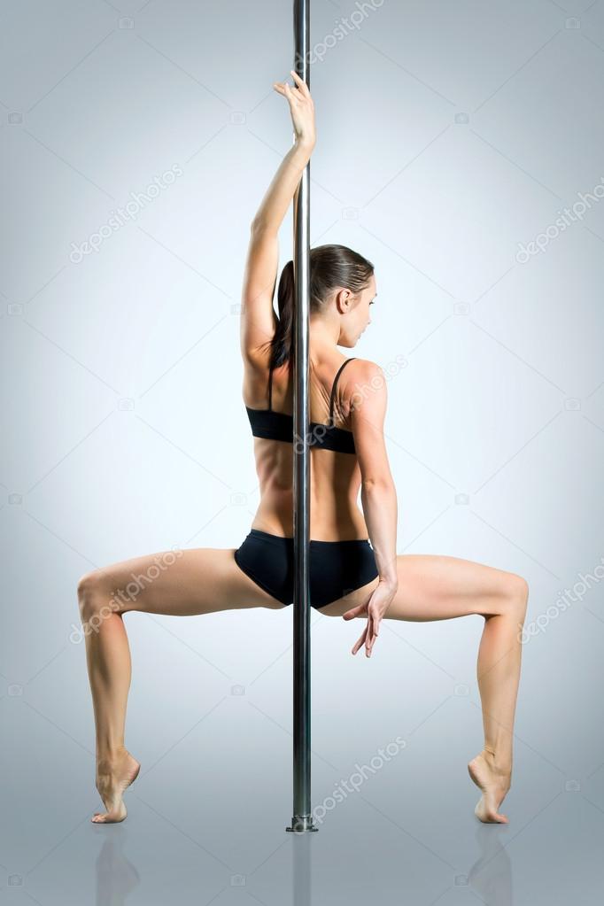 Young sexy woman exercise pole dance against a gray background