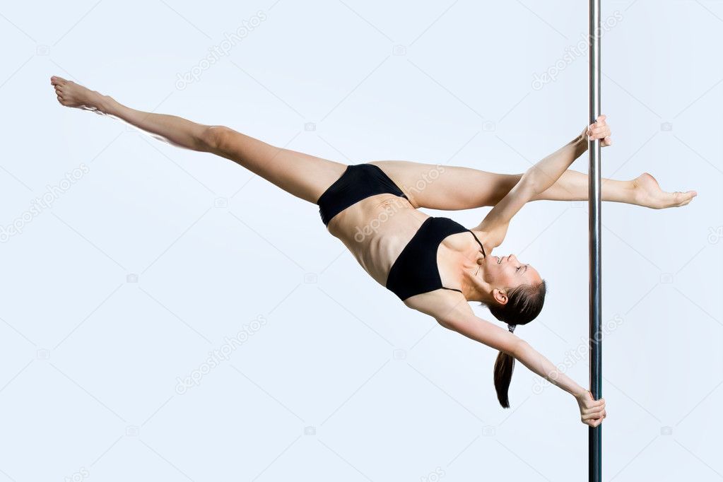 Young sexy woman exercise pole dance against a gray background