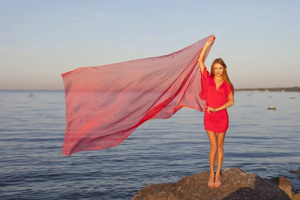 Una joven con un vestido rojo de pie en la orilla — Foto de Stock