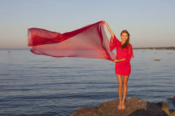 Een jong meisje in een rode jurk staande op de oever — Stockfoto