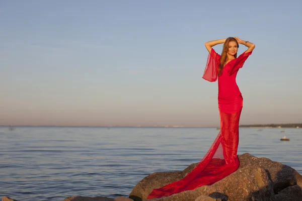 Una joven con un vestido rojo de pie en la orilla — Foto de Stock