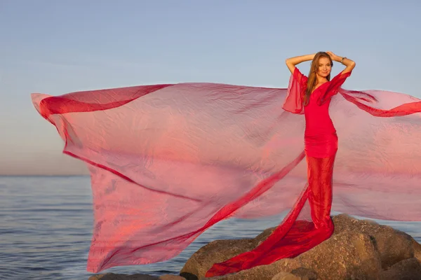 En ung flicka i en röd klänning som står på stranden — Stockfoto
