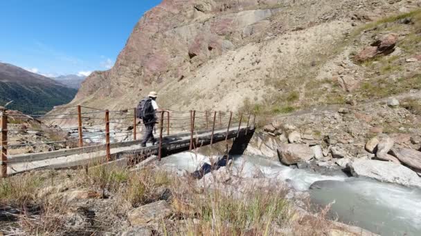 Пеший турист, пересекающий небольшой мост через высокогорный поток — стоковое видео