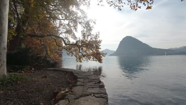 Passeio Marítimo do Lago de Lugano com árvores de outono vermelhas e laranja ao nascer do sol — Vídeo de Stock