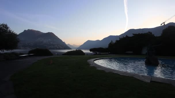 Nascer do sol no Lago Lugano visto de um jardim com uma fonte — Vídeo de Stock