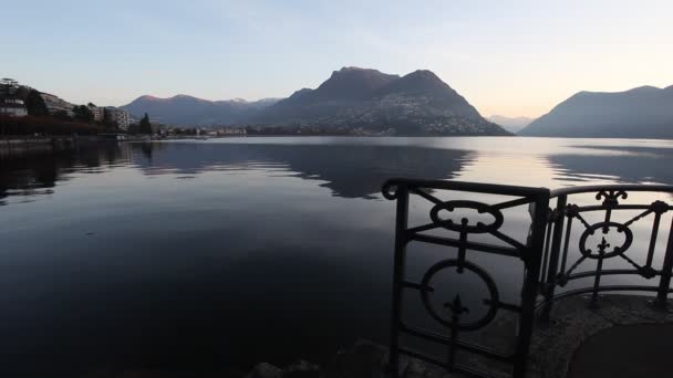 Salida del sol en el lago Lugano con vistas hacia la ciudad y la frontera suiza italiana — Vídeo de stock