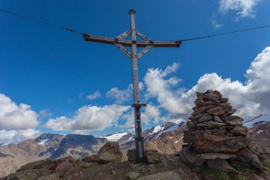 Alp zirvesi haçlı ve arkasında buzullar olan taş yığınları.