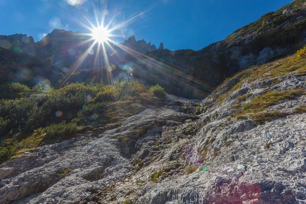 Sun rays filter between the Dolomite peaks in Comelico region over a small waterfall, Dolomites, Italy. Backlight photo with flare