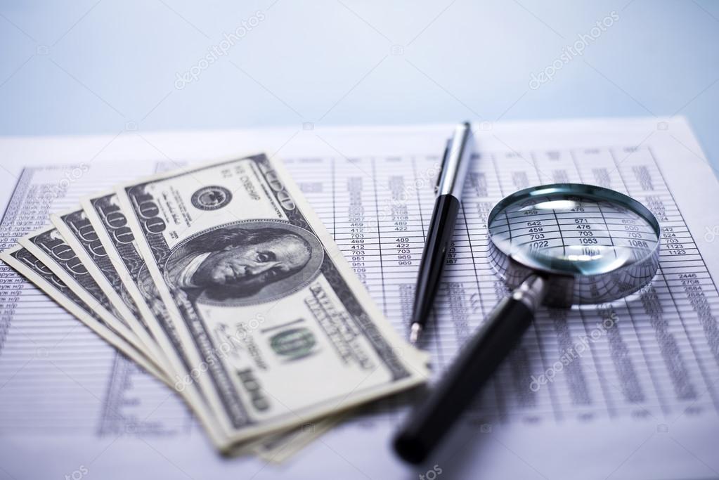 Dollars with a magnifying glass, pen and report