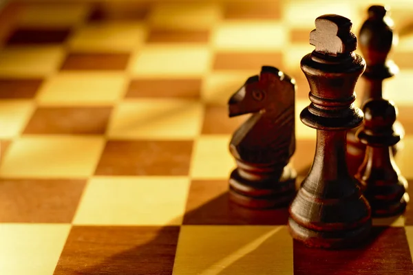 Tmavé dřevěné šachové figurky v paprsku světla — Stock fotografie