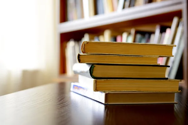 Pile of books with bookshelves in the background — Stock Photo, Image