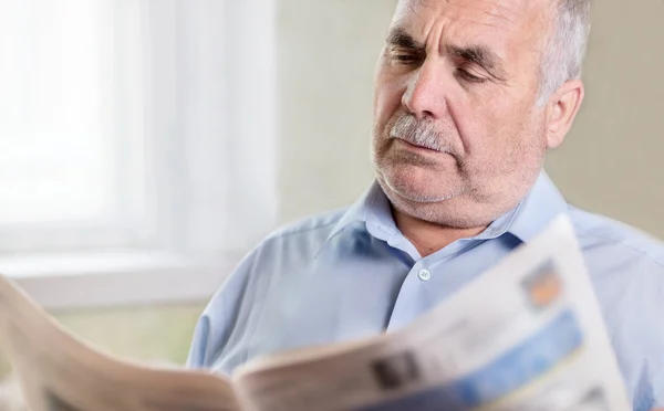 Senior Caucasian man reading a newspaper at home — Stock Photo, Image