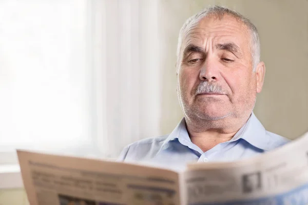 Senior Caucasian man reading a newspaper at home — Stock Photo, Image