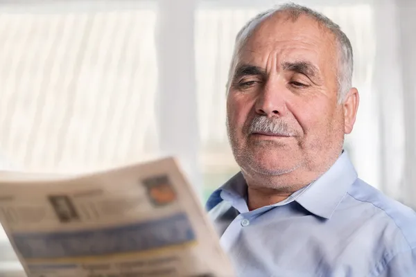 Senior Caucasian man reading a newspaper at home — Stock Photo, Image
