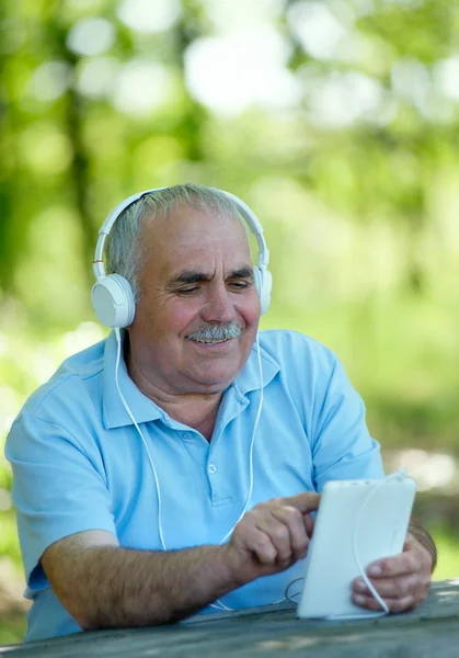 Senior man smiling happily as he listens to music — Stock Photo, Image