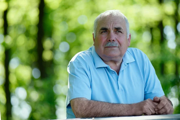 Elderly man sitting outdoors smiling at the camera — Stock Photo, Image