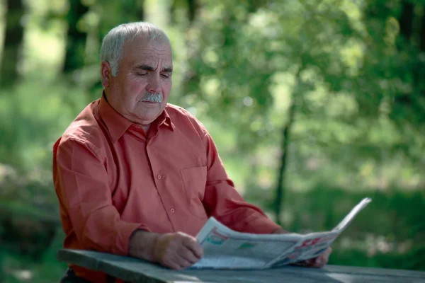 Senior man sitting reading a newspaper — Stock Photo, Image