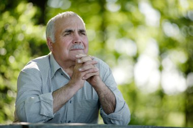 Elderly man sitting in the garden thinking clipart