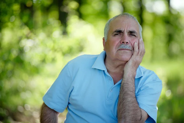 Elderly man sitting outdoors smiling at the camera — Stock Photo, Image