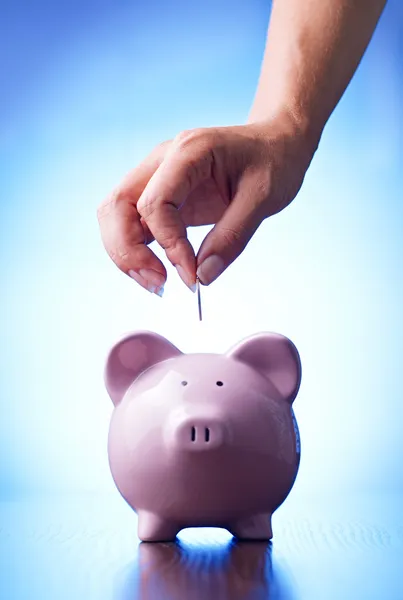 Mão colocando uma moeda em um banco porquinho — Fotografia de Stock