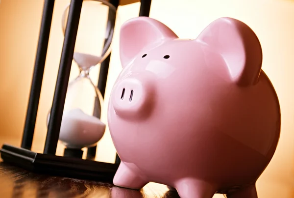Pink piggy bank with a vintage hourglass behind — Stock Photo, Image
