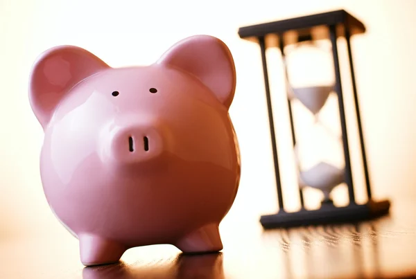 Roze piggy bank met een vintage zandloper achter — Stockfoto