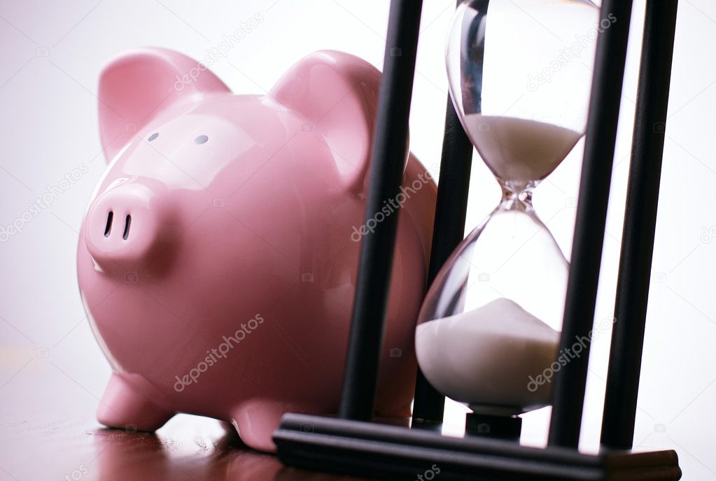 Pink piggy bank with a vintage hourglass behind