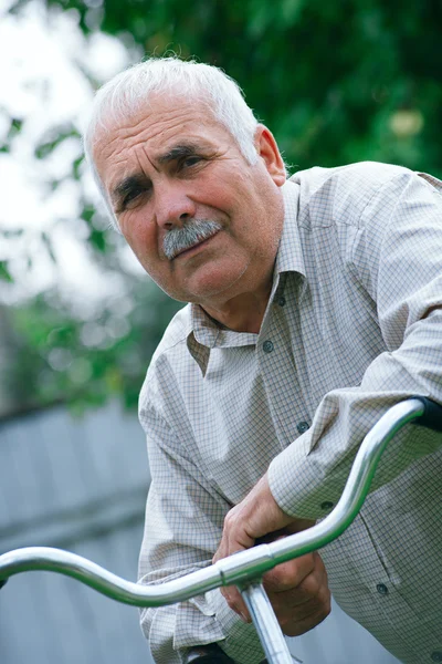 Senior man leaning on the handlebar of his bicycle — Stock Photo, Image