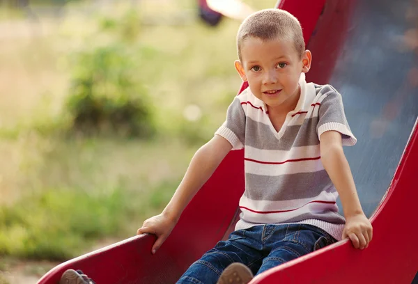Piccolo ragazzo che gioca su uno scivolo in un parco giochi per bambini — Foto Stock