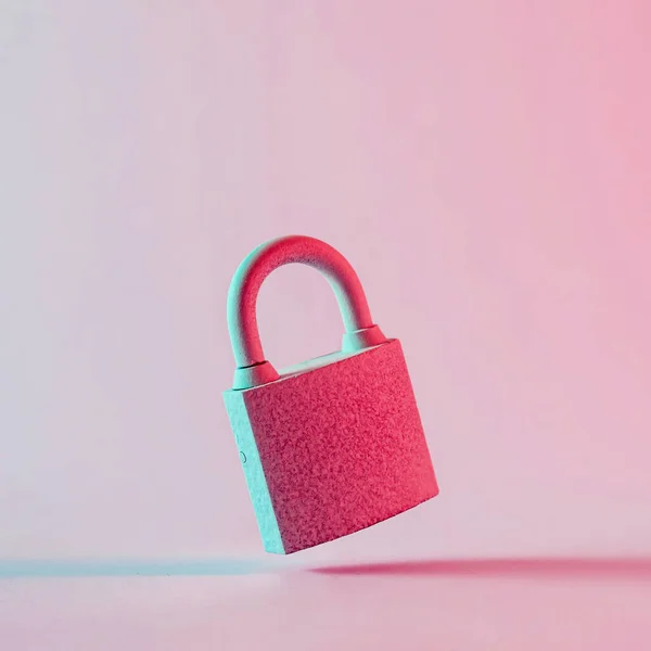 セキュリティや個人情報のシンボルとしてコピースペースのためのピンクのスタジオの背景に浮かぶ古い錆びた塗装南京錠のクローズアップ — ストック写真