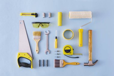 Çekiç, testere, gözlük, bant, boya fırçaları ve silindir ve geri çekilebilir bıçakla mavi üzerine çeşitli DIY araçları düz yatıyordu