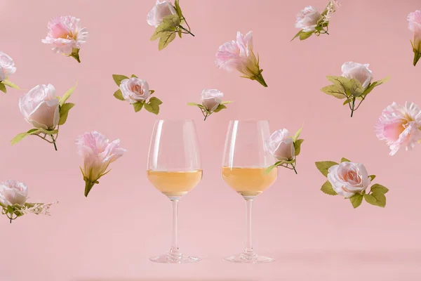 Two glasses of white wine on pink background and falling rose flowers. Concept of holiday party wedding or Valentine