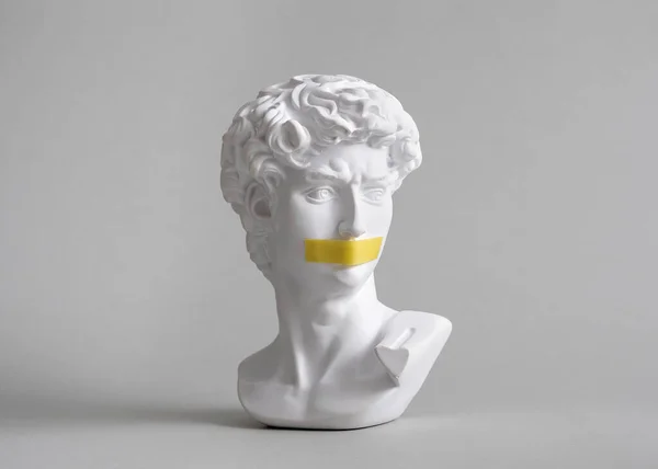 Michelangelo\'s David head bust in duct tape sealed mouth. Minimal concept on gray background censorship of freedom of speech and restrictions of thought and word. Fight for your rights.