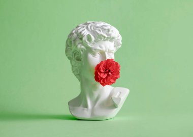Michelangelo's David head sculpture with rose flower closed mouth. Minimal pastel creative kiss and love concept.