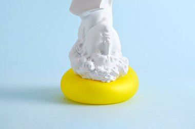 David statue plaster upside down presses on the yellow balloon. Minimal surreal pastel creative concept.