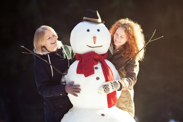 Due giovani donne abbracciano pupazzo di neve — Foto Stock