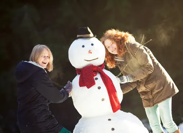 Dos mujeres jóvenes construyendo un muñeco de nieve — Foto de Stock